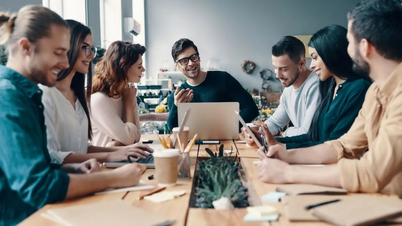 Digital marketing team collaborating around a table with laptops, tablets, and coffee cups in a modern office.